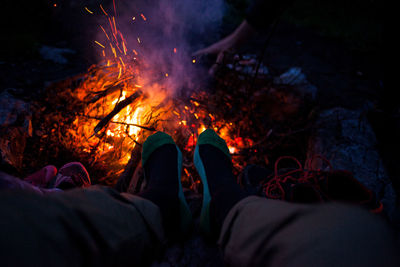 Low section of person sitting by campfire at night