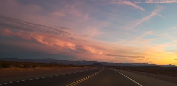 Empty road along landscape at sunset