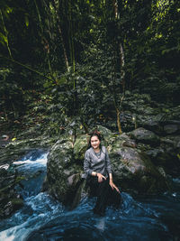 Young woman sitting on rock in forest