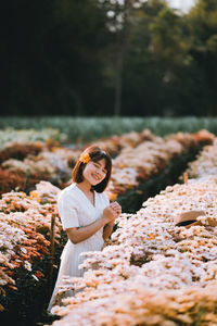 Smiling woman standing by flowering plants on field