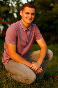 Happy people. portrait of smiling young brunette man in purple polo shirt seating outdoor on nature