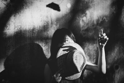 Young woman holding sunhat and gesturing against wall