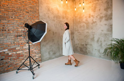 Portrait of young woman standing by wall at studio