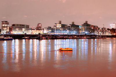 Boats in river by illuminated buildings in city at night