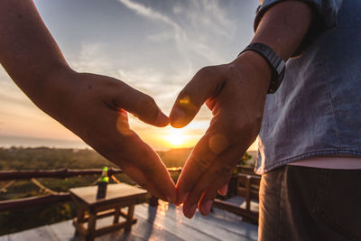 Close-up of hands shaping heart during sunset