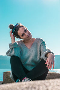 Young woman sitting on retaining wall against clear sky