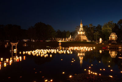 Illuminated temple by lake against sky at night