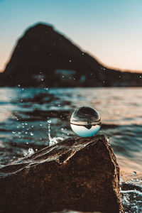 Close-up of crystal ball on rock by sea