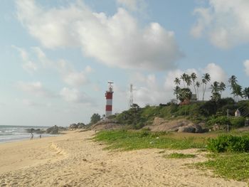 Lighthouse on beach by sea against sky