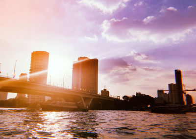 Bridge over river by buildings against sky during sunset