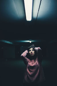 Woman with hand in hair looking at illuminated light while standing in dark parking lot
