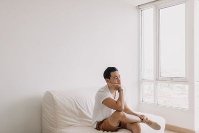 Young woman using mobile phone while sitting on bed at home