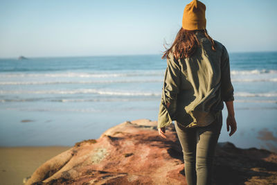 Rear view of woman standing on rock at beach against sky