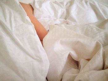 Person covered with blanket and pillow resting on bed