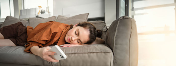 Young woman using mobile phone while lying on bed at home