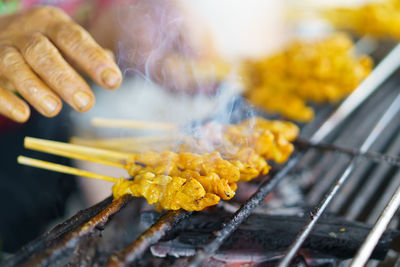 Close-up of hand holding meat on barbecue grill