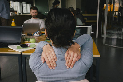 Rear view of exhausted businesswoman rubbing shoulders while sitting at workplace