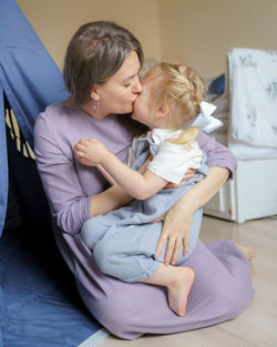 Mother expressing love to little daughter while sitting in kids room