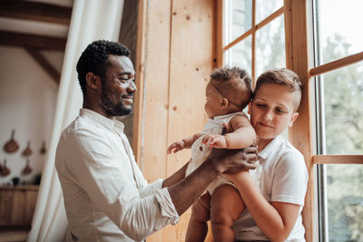 Full length of father and daughter sitting on window at home