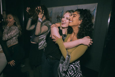 Cheerful young women embracing while enjoying at nightclub