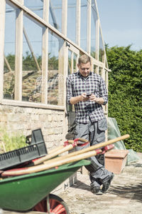 Man using smart phone while leaning on greenhouse at community garden