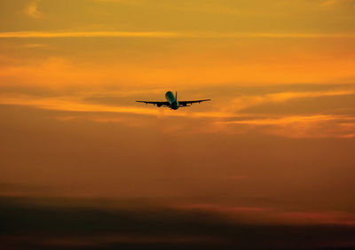 Silhouette airplane flying against dramatic sky during sunset