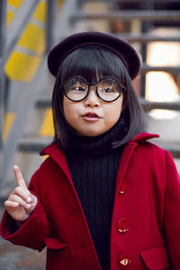 Korean girl in a red coat and cap and round glasses stands on the iron staircase the street