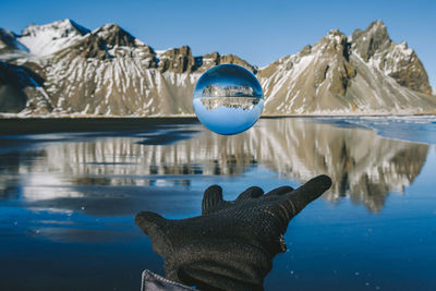 Cropped hand with crystal ball in mid-air against lake and mountain