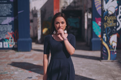 Portrait of young woman standing in city against built structures