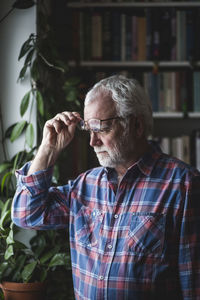 Thoughtful senior therapist standing by potted plant at home office