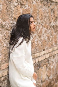 Side view of a young woman looking away against wall