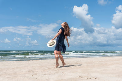 Full length of young woman standing at beach against sky