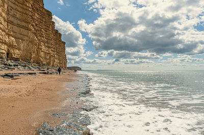 Distant view of mother and kids walking on beach by rock formation against sky