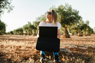 Woman using laptop while sitting at olive orchard