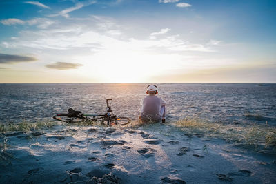 Man sitting at beach against sky during sunset