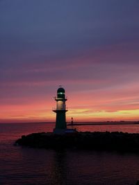 Lighthouse by sea against sky during sunset