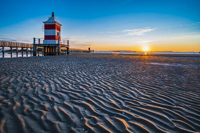 The sun rises over the calm waters of lignano sabbiadoro. explosion of colors on the red lighthouse.