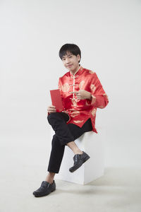 Full length portrait of smiling man sitting on floor against white background