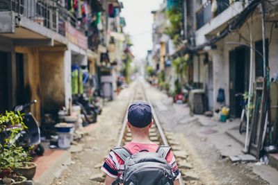 Rear view of man with backpack standing on railroad track amidst houses