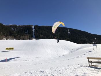 Person paragliding on snowcapped mountain against sky