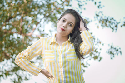 Portrait of smiling young woman standing against trees and sky