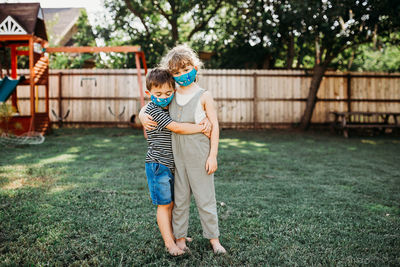 Two kids hugging and standing outside wearing homemade fabric masks