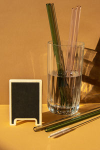 Reusable glass straws in glass with water on beige neutral background with label for your text low