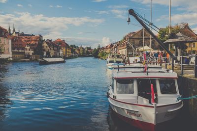 Boats moored in canal by town against sky