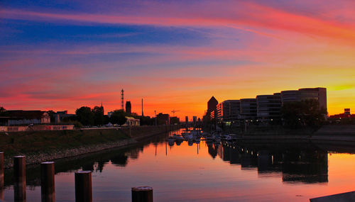 River amidst silhouette buildings against sky during sunset