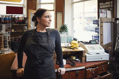 Smiling cashier standing while looking away in workshop