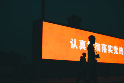 Silhouette people standing against illuminated wall at night