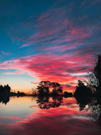 Silhouette trees by lake against sky during sunset