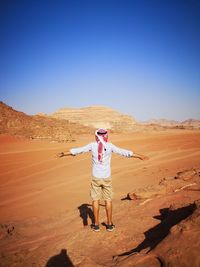Rear view full length of man with arms outstretched standing at desert on sunny day