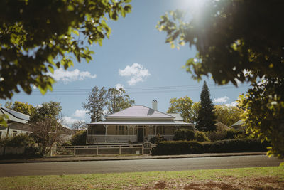 House by trees on field against sky on sunny day